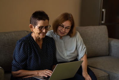 Smiling senior women sitting at home office workplace looking in laptop.