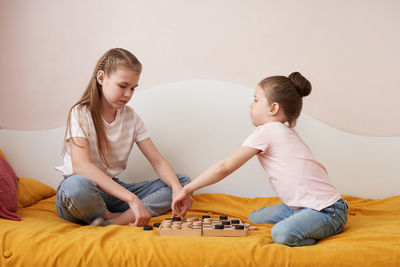 Sisters playing draughts board game on bed