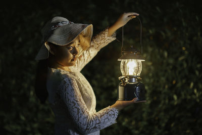 Close-up of woman holding hat against black background