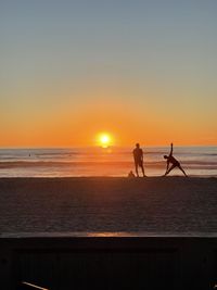 Silhouette people on beach against sky during sunset