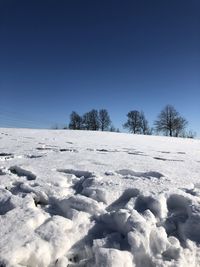 Snow covered field against clear blue sky