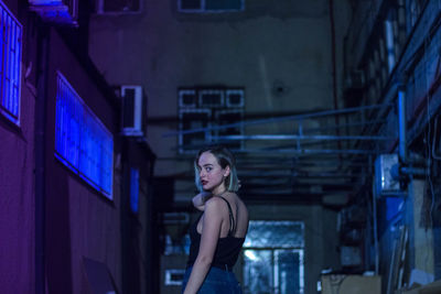 Portrait of young woman standing against illuminated building at night