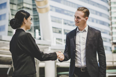 Business people giving handshake while standing against building in city