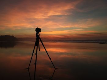 Silhouette person standing by lake against sky during sunset