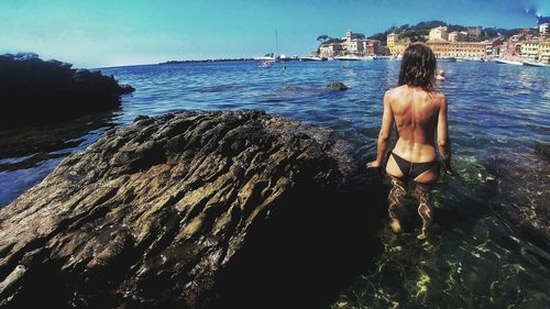 Rear view of shirtless woman standing at sea shore against sky