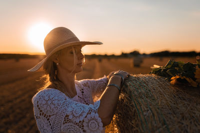 Woman looking at straw bale against sky during sunset