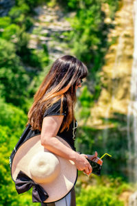 Side view of woman holding smart phone while standing outdoors