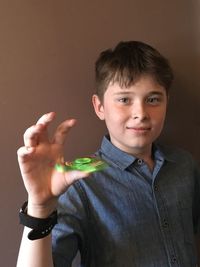 Portrait of boy spinning fidget spinner against brown wall