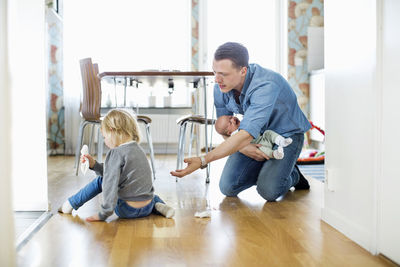 Father holding baby girl while cleaning floor with daughter at home