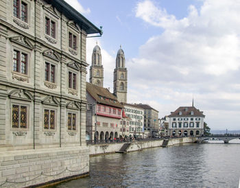 View of buildings by river against cloudy sky