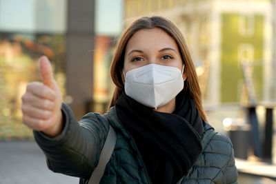 Portrait of young woman wearing mask gesturing outdoors