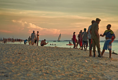 People at beach against sky during sunset