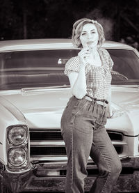 Attractive woman dressed in pin-up style, leaning on an old vintage car, in black and white