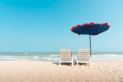 Sunshade and lounge chairs on beach against clear blue sky