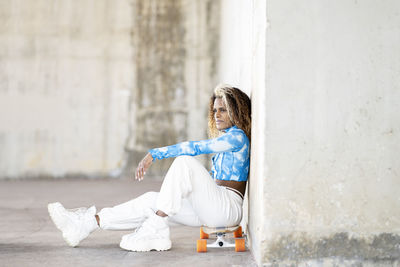 Side view of woman sitting against wall