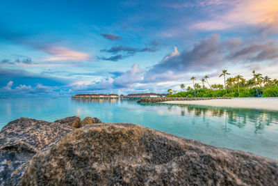 Scenic view of turquoise water bay in maldives against dramatic sunset sky