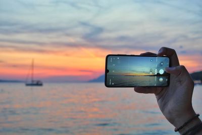 Man photographing sea against sky during sunset