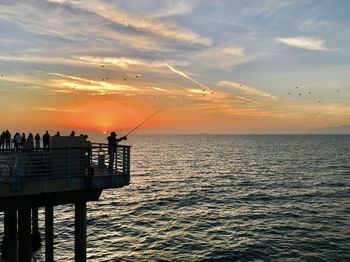 Silhouette fishing rod on sea against sky during sunset