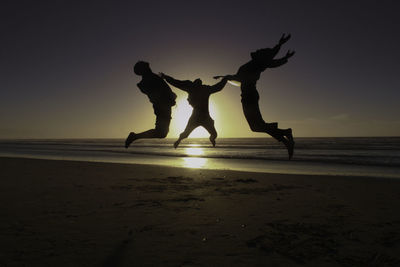 Silhouette people jumping on beach against sunset