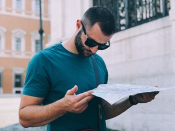 Mid adult man reading map while standing against buildings in city