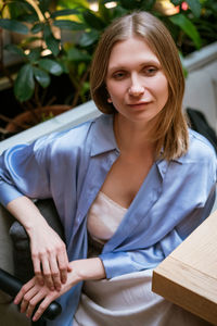 Blonde woman is sitting at a table in a cafe, wearing a blue shirt and looking at the camera.