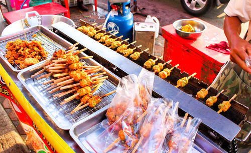 Person preparing food skewers on barbecue grill at market