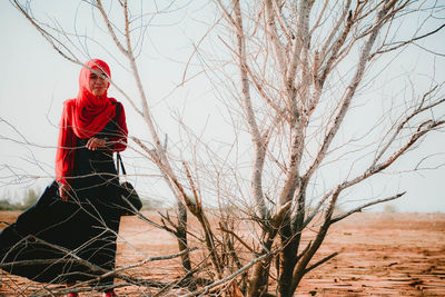 Woman in hijab standing by bare tree on land