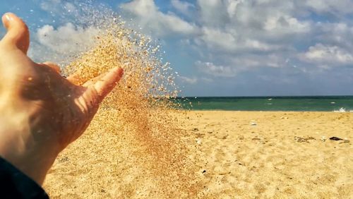 Close-up of hands on sand at beach against sky