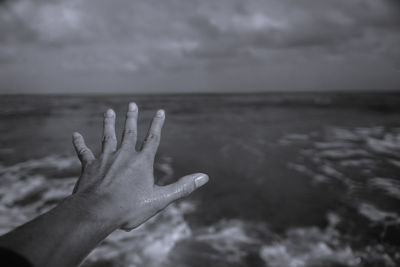 Cropped image of hand against sea against sky