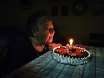 Woman blowing burning candles on cake in the dark