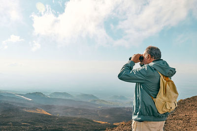 Rear view of woman photographing on mountain against sky