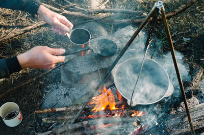 Cropped hands of man preparing food on fire at campsite