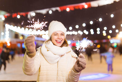 Portrait of smiling woman standing against illuminated wall during winter