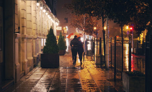 Rear view of couple walking on street during monsoon night