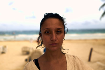 Portrait of young woman standing at beach against sky