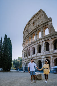 Couple holding hands in front of historical building against sky