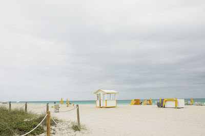 Beach hut at shore against cloudy sky