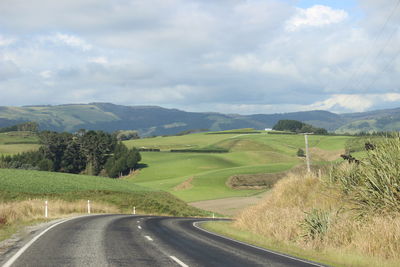 Hilly windy road amidst green field against sky