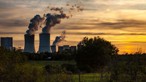 Smoke emitting from factory against sky during sunset