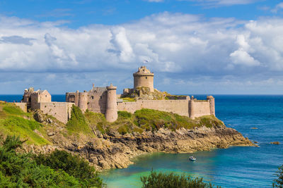 Buildings by sea against cloudy sky