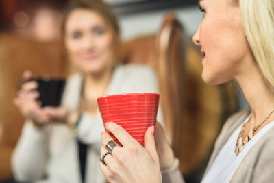 Crop woman enjoying hot drink near friend