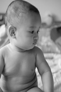 Cute shirtless baby girl sitting on bed at home