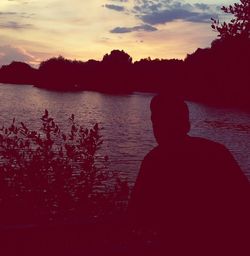 Silhouette man looking at lake against sky during sunset