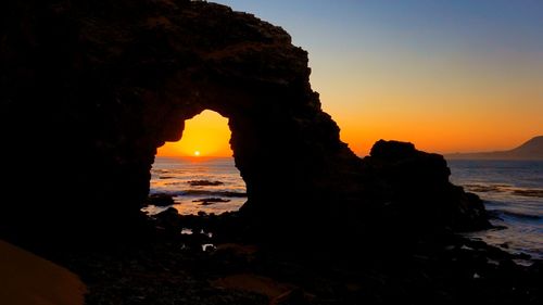 Silhouette rock formation on beach against sky during sunset