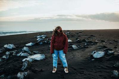 Woman standing on rock at beach against sky