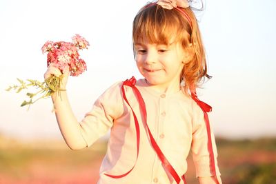 Smiling girl with pink flowers standing on land