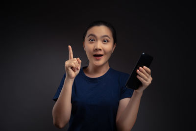Portrait of young woman using mobile phone against black background