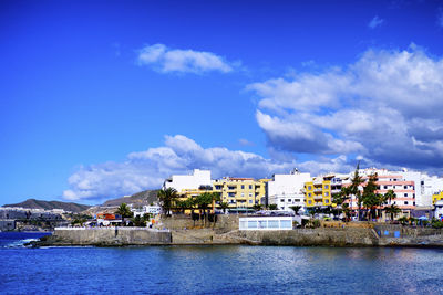 Buildings by sea against blue sky