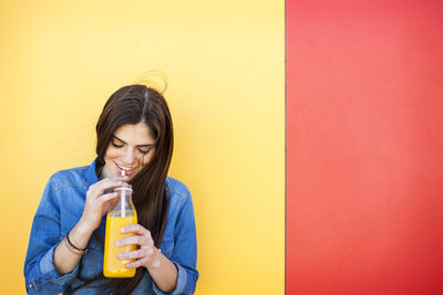 Young woman drinking glass against yellow wall