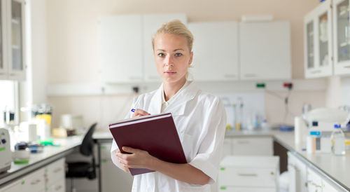 Portrait of woman writing in book standing in laboratory